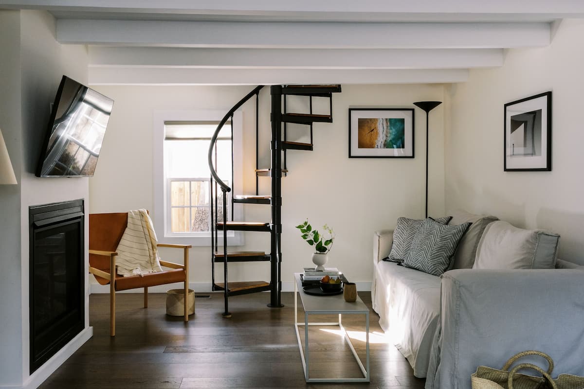 A modern living room with a fireplace, a wooden chair, a sofa, a coffee table, and a spiral staircase.