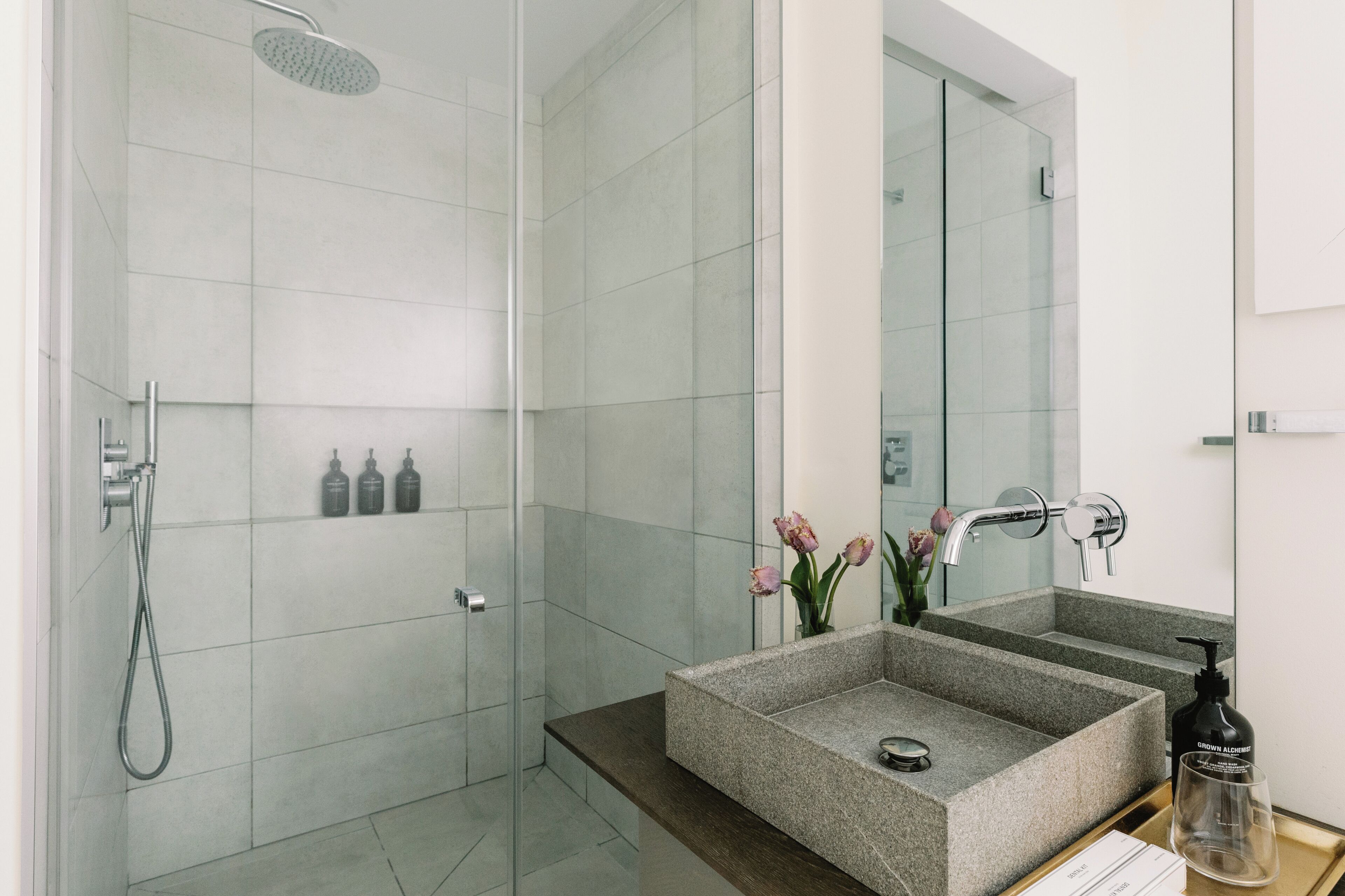 A modern bathroom with a glass-enclosed shower, a granite sink, and a large mirror.