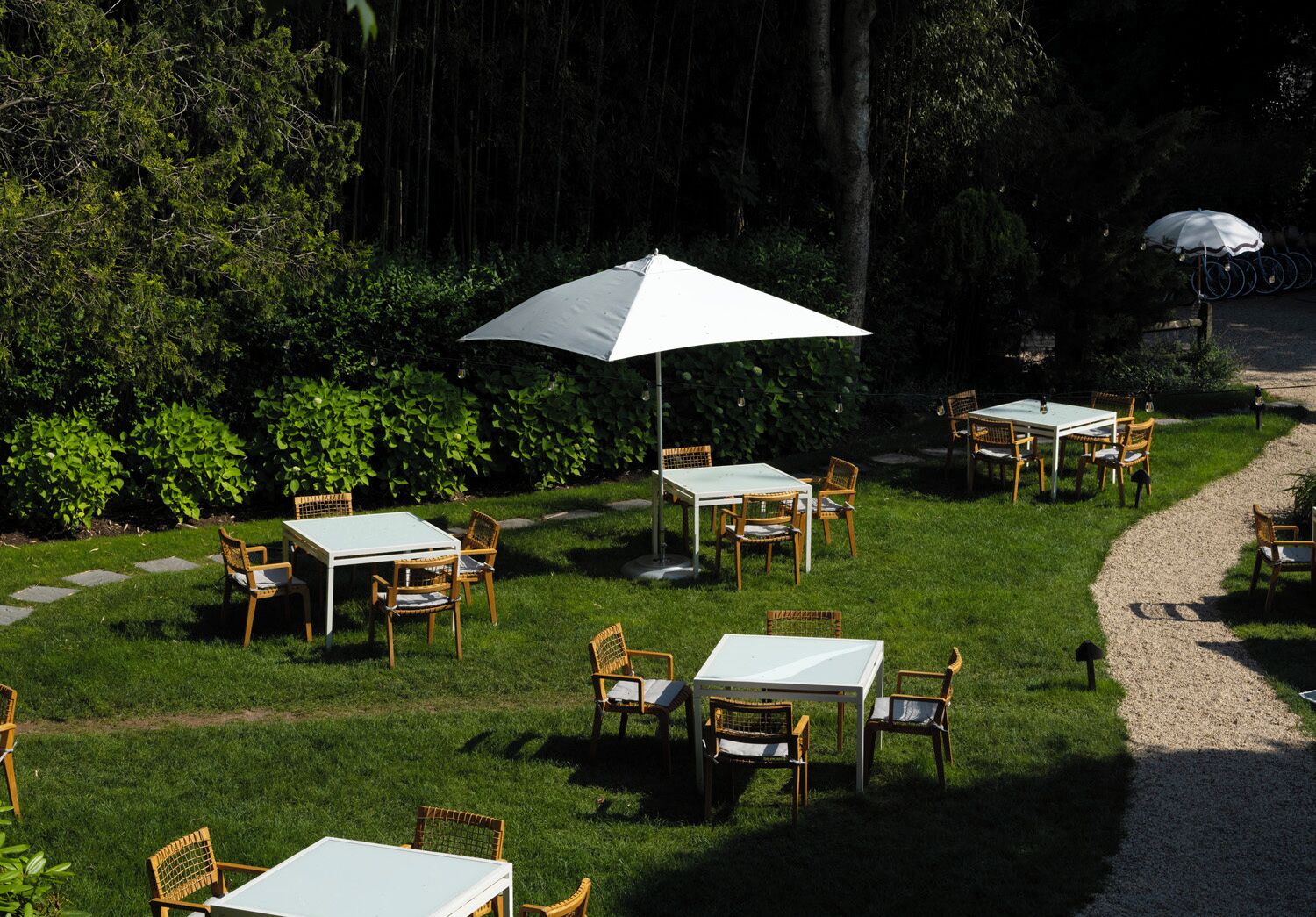 Un área de comedor al aire libre con mesas y sillas, rodeada de abundante follaje y árboles.