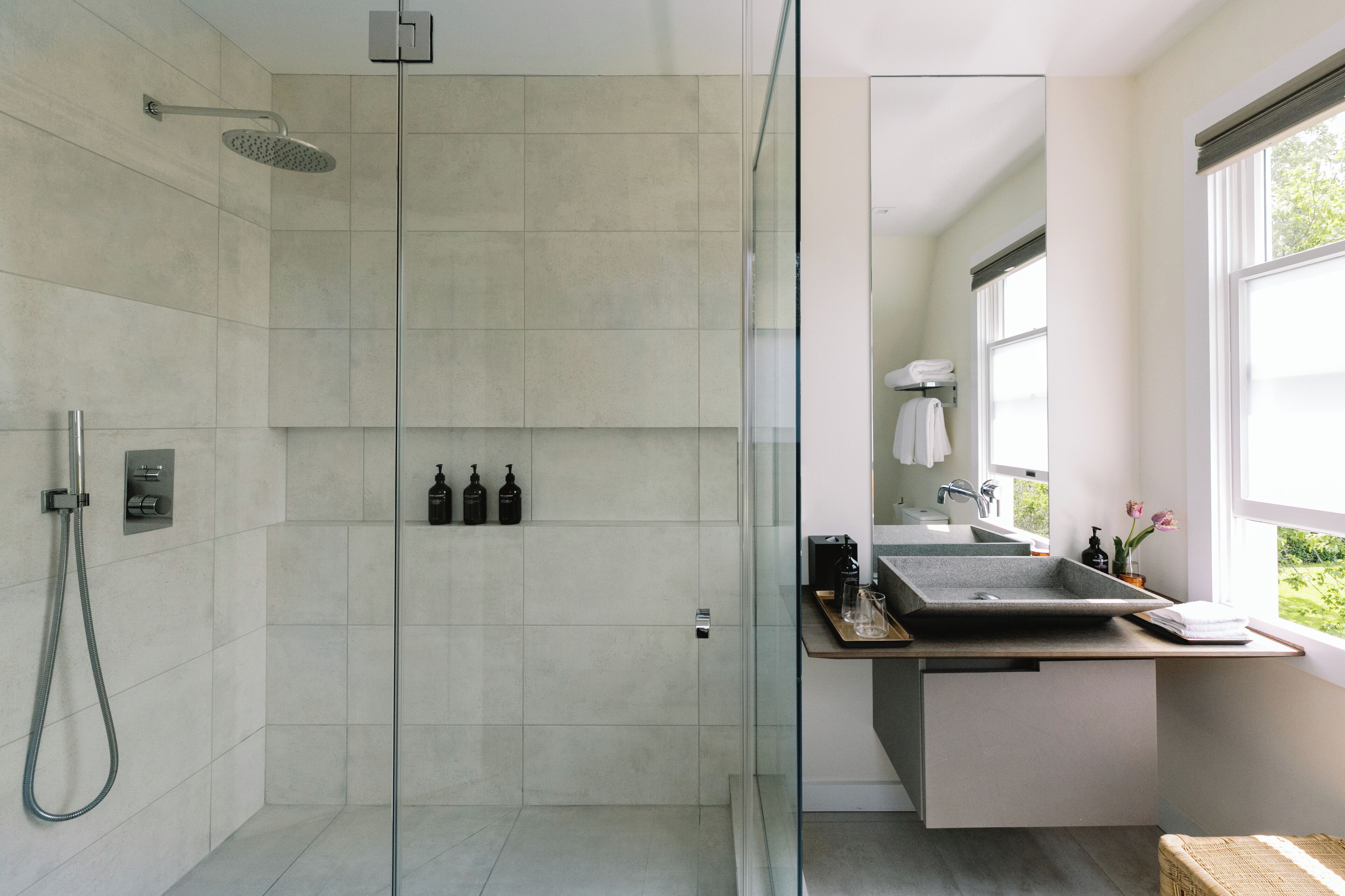 Un baño moderno con ducha envuelta en vidrio, un lavabo con una amplia pila y un ventanal que proporciona luz natural.