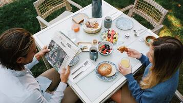 A table set outdoors with various breakfast items, including bread, fruit, and beverages.