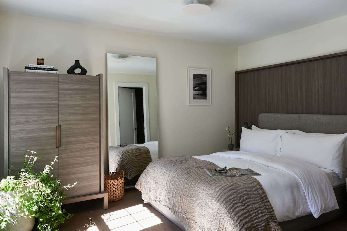 A bedroom with a bed, a wardrobe, a mirror, and a potted plant.