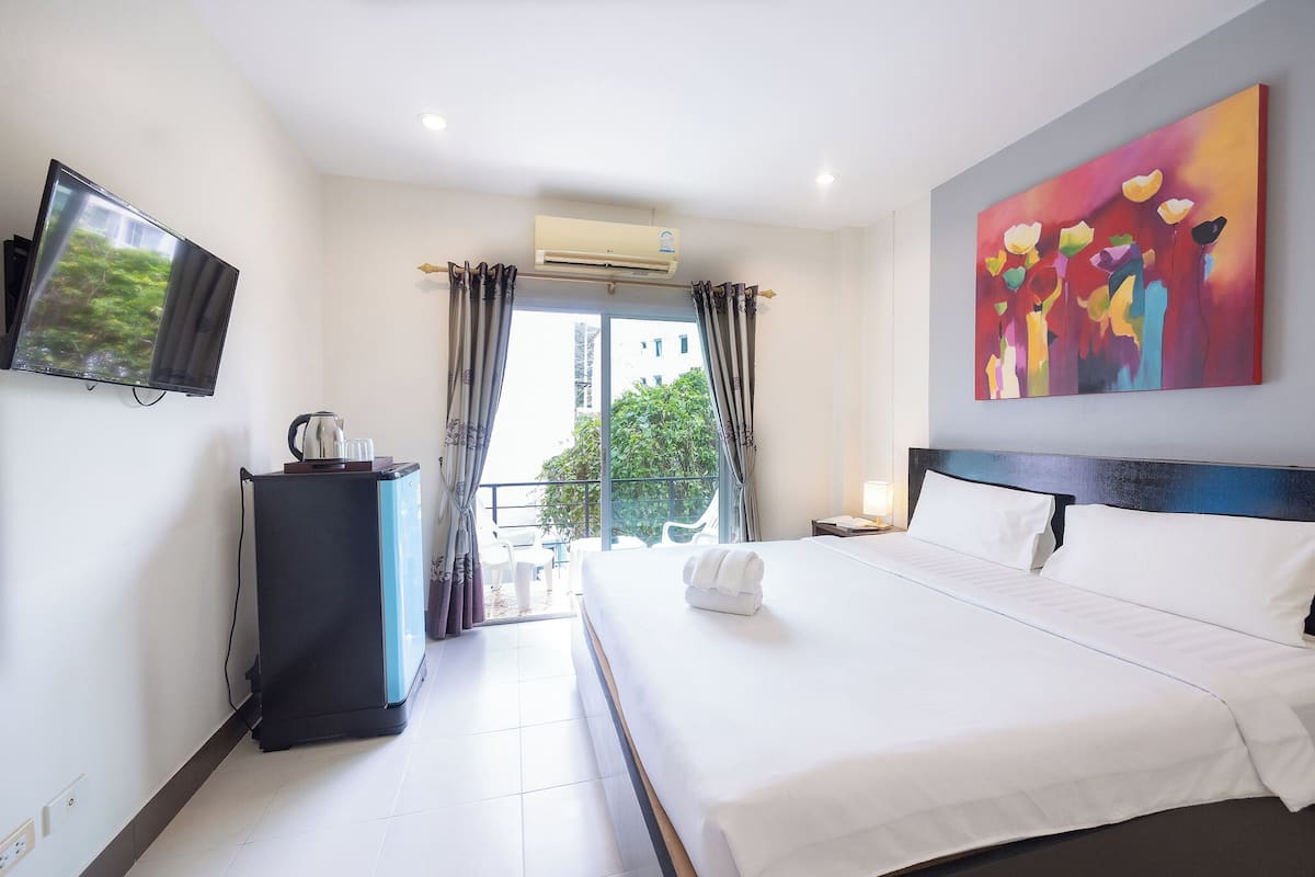 A hotel room with a bed, a flat-screen TV, a coffee machine, and a painting on the wall.