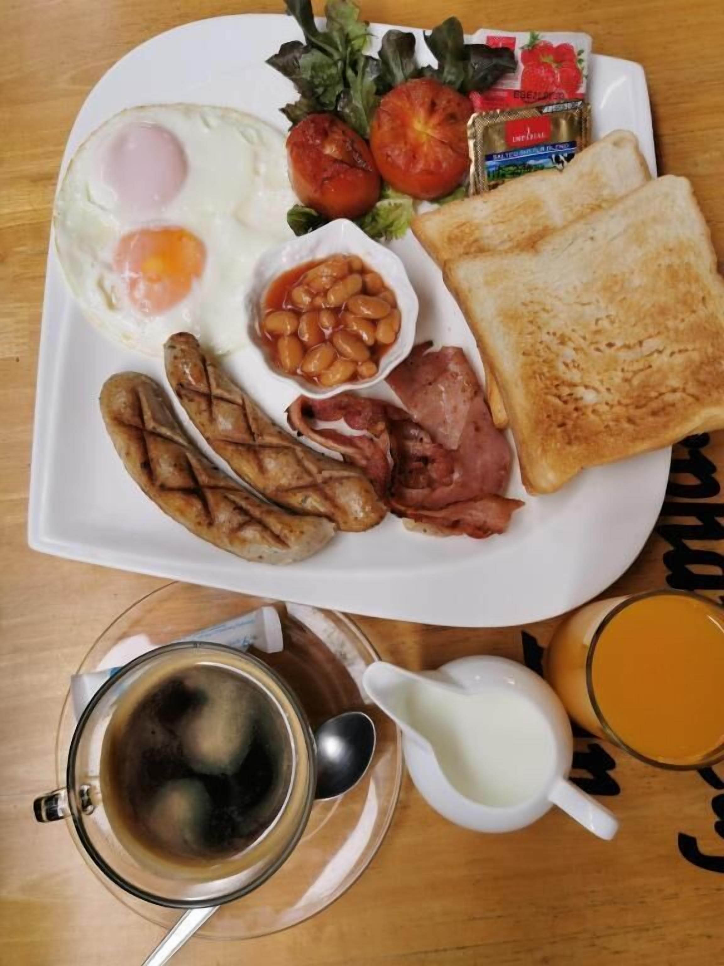 A breakfast plate with eggs, sausages, bacon, toast, tomatoes, and beans.