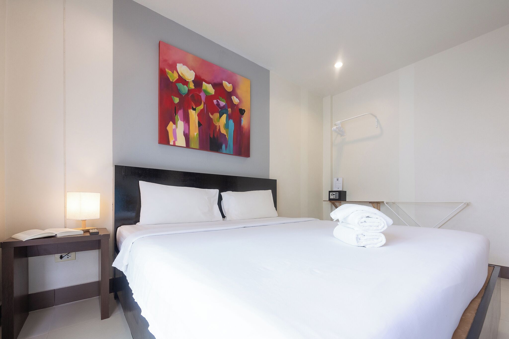 A hotel room with a large bed, a nightstand with a lamp, a painting on the wall, and a towel on the bed.