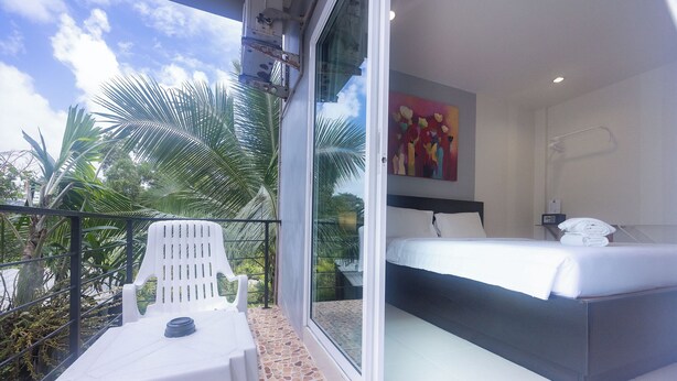 Un balcón con una silla y una mesa blancas, una cama con ropa de cama blanca y un cuadro en la pared.