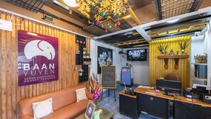 Una zona de recepción con un sofá marrón, un escritorio con una computadora y un letrero que dice "BAAN YUEN".