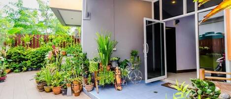 A modern building with a large glass door, surrounded by various potted plants and a small garden area.