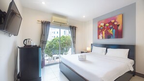 Habitación de hotel con una cama grande, un televisor de pantalla plana, cafetera y balcón con vistas a edificios y zonas verdes.