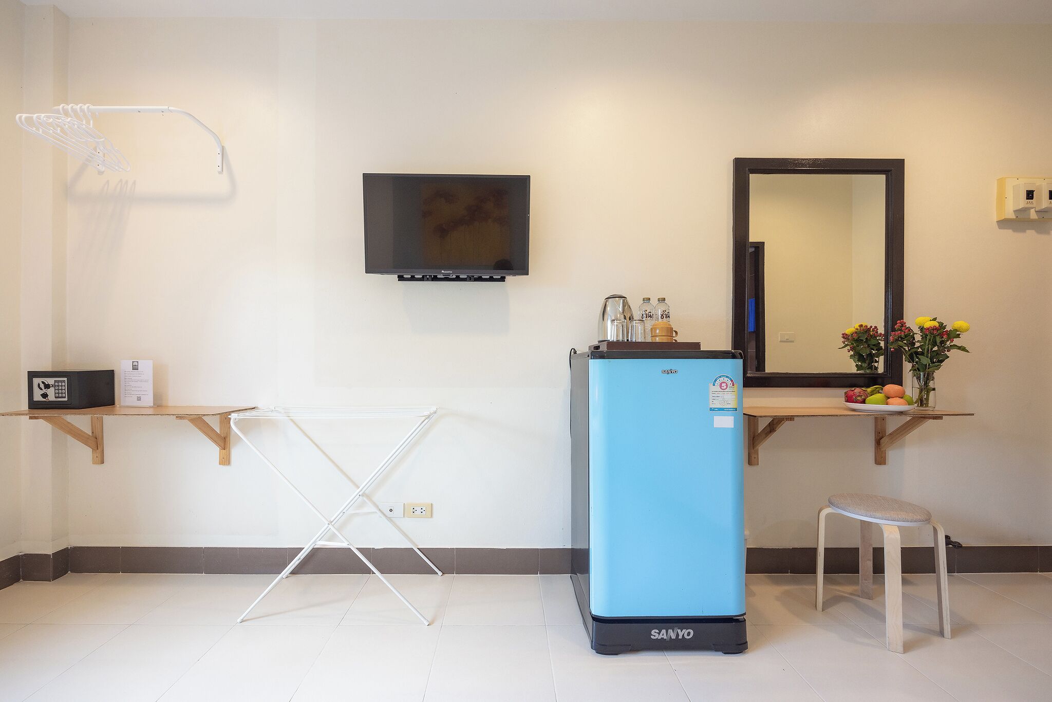 A hotel room with a blue refrigerator, a TV mounted on the wall, a small stool, and a mirror above the counter.