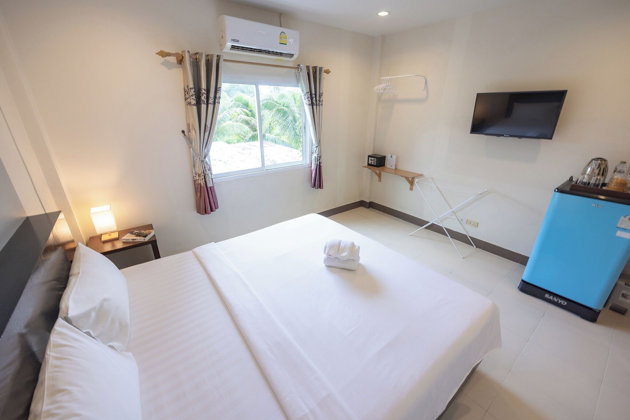 A hotel room with a bed, a TV, a minibar, and a window with curtains.