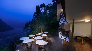 An outdoor deck with wooden flooring, multiple tables and chairs, and white umbrellas providing shade. - Cilan Resort (Datong)