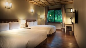 A hotel room with two beds, wooden flooring, a desk with a chair, a window with a view of trees, and wall-mounted lamps. - Cilan Resort (Datong)
