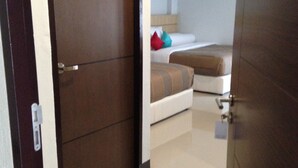 A hotel room with a wooden door, a bed with a beige headboard, and a small bedside table. - The Rama Residence Chiang Rai (Chiang Rai)