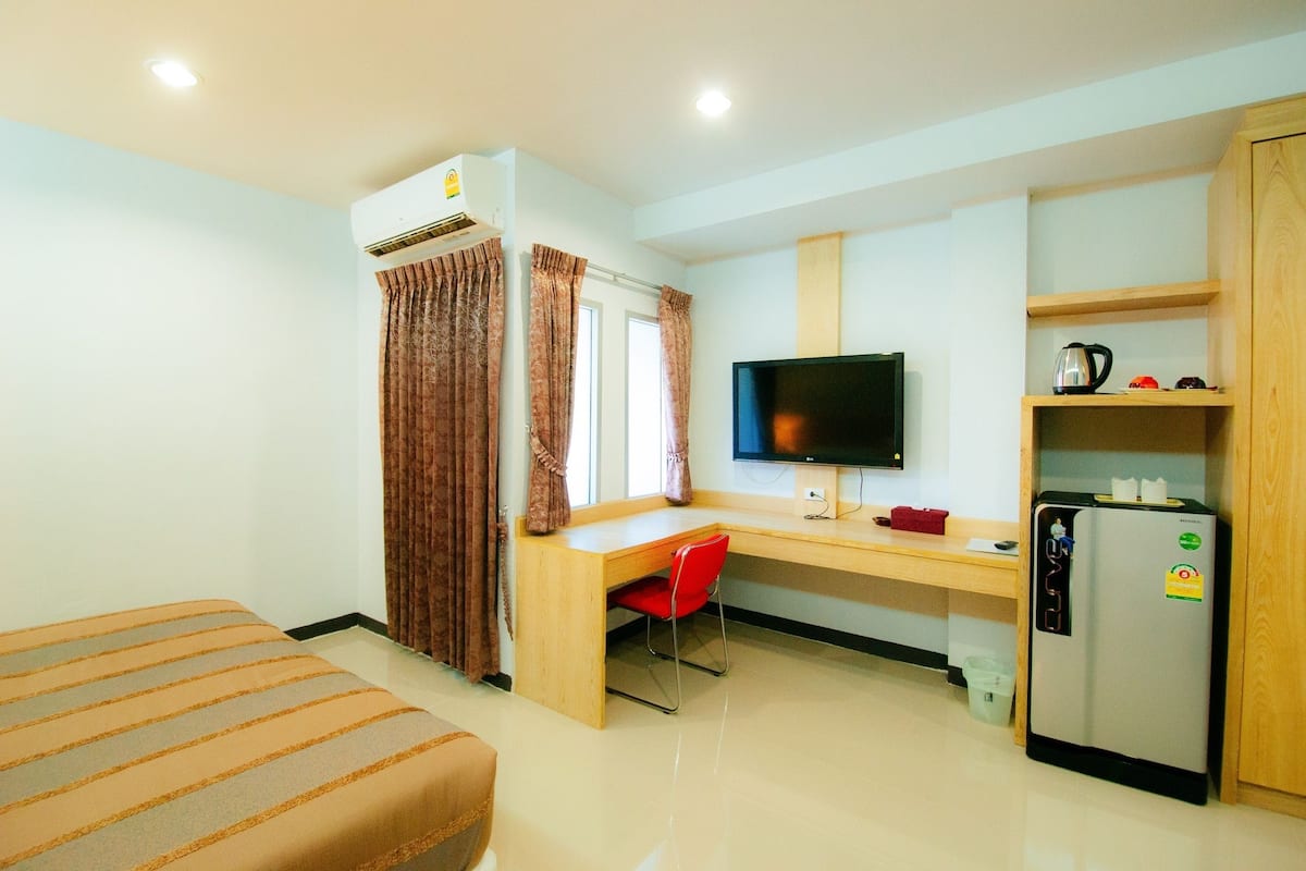 Habitación de hotel compacta con cama, escritorio con silla, televisor, refrigerador y ventana con cortinas.