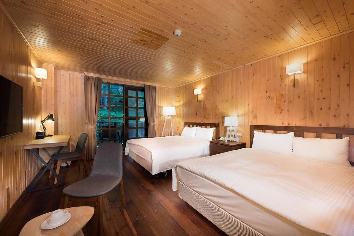 Ein Zimmer mit Holzwänden, zwei Betten, einem Schreibtisch, einem Stuhl und einem Fernseher.