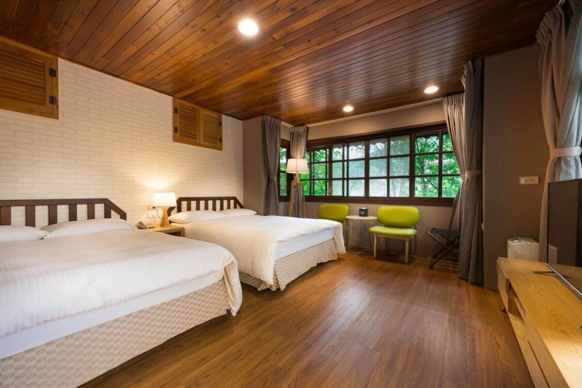 Ein Hotelzimmer mit zwei Betten, Holzboden, einem Fenster mit Vorhängen, einem kleinen Tisch und einem Stuhl.