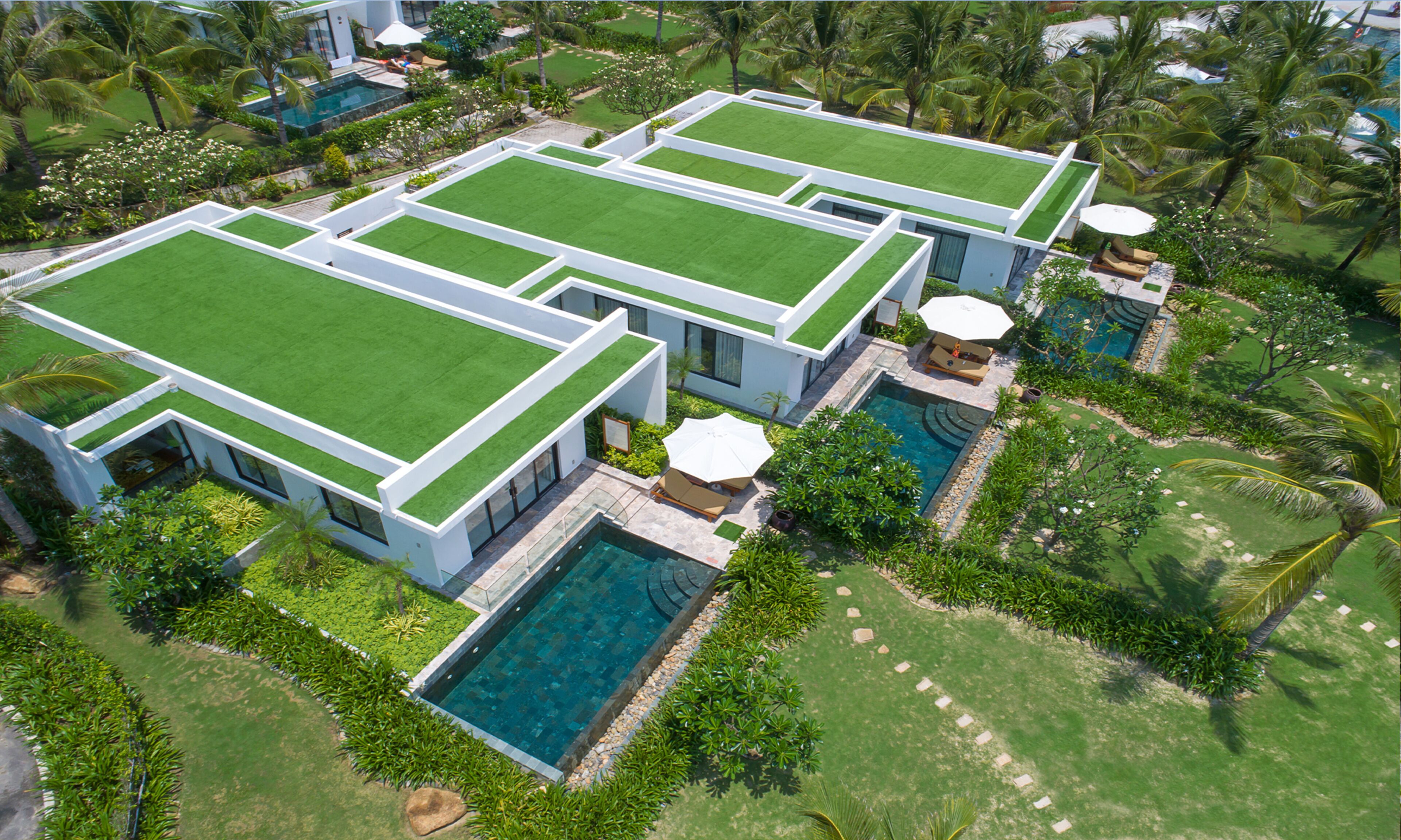 A modern resort with multiple buildings, a swimming pool, and lush greenery.