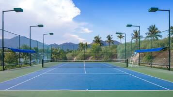 A tennis court with a net, surrounded by a fence, and palm trees in the background.