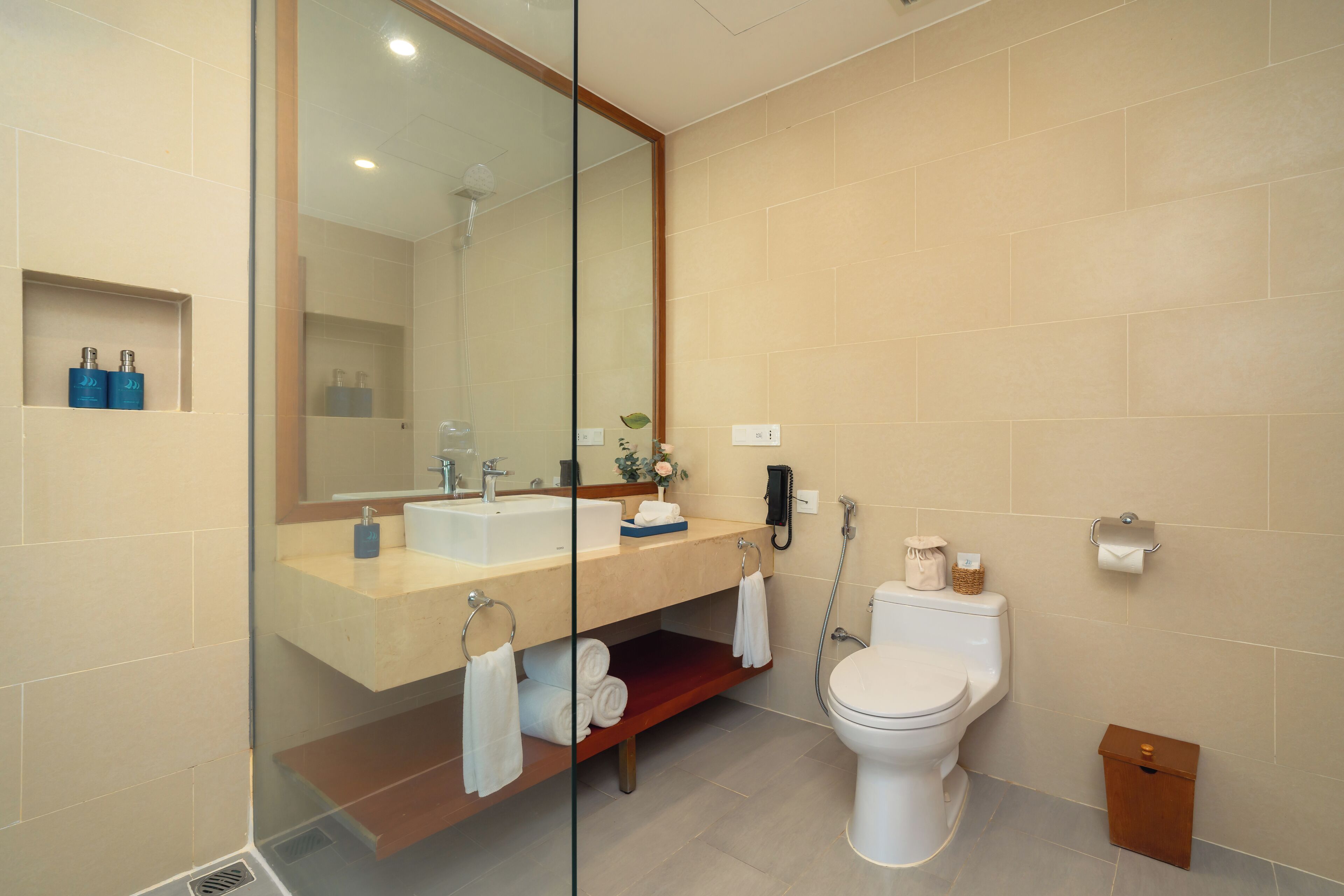 A modern bathroom with a glass-enclosed shower, a white toilet, and a beige tiled wall.