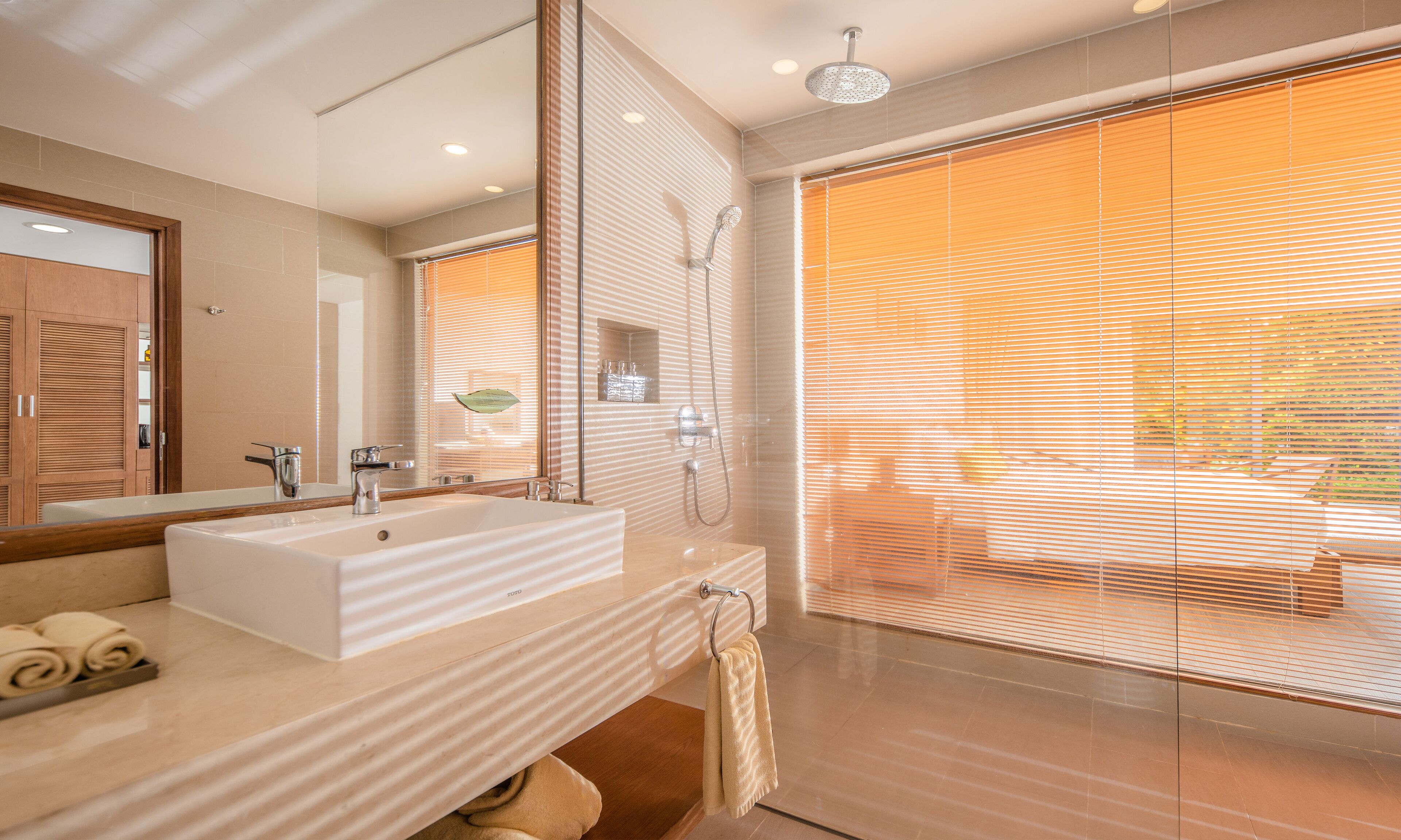 Une salle de bain moderne avec un grand miroir, un lavabo blanc et une douche séparée par des parois en verre.