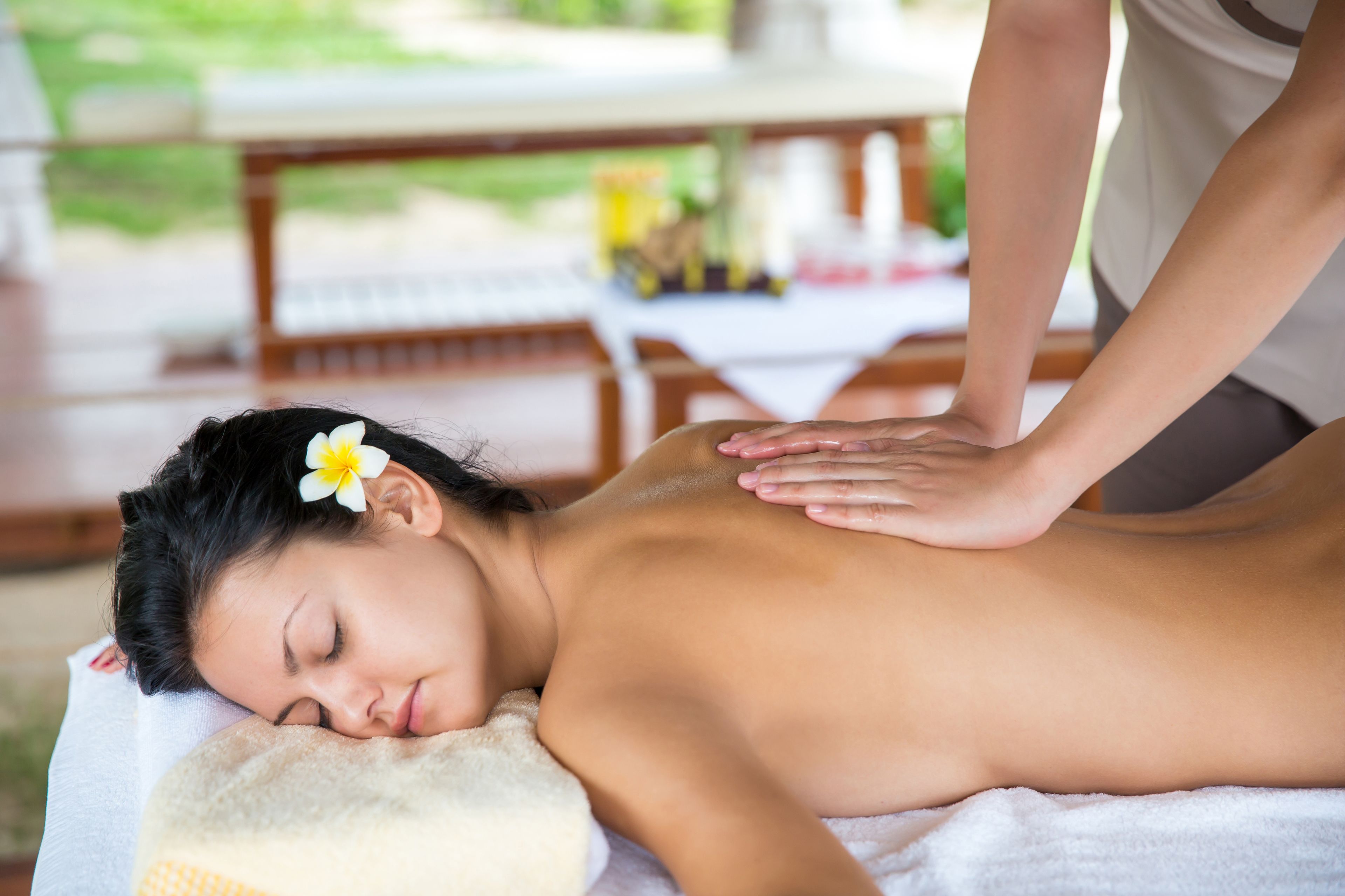 A person receiving a back massage in a room with a wooden table and chairs in the background.