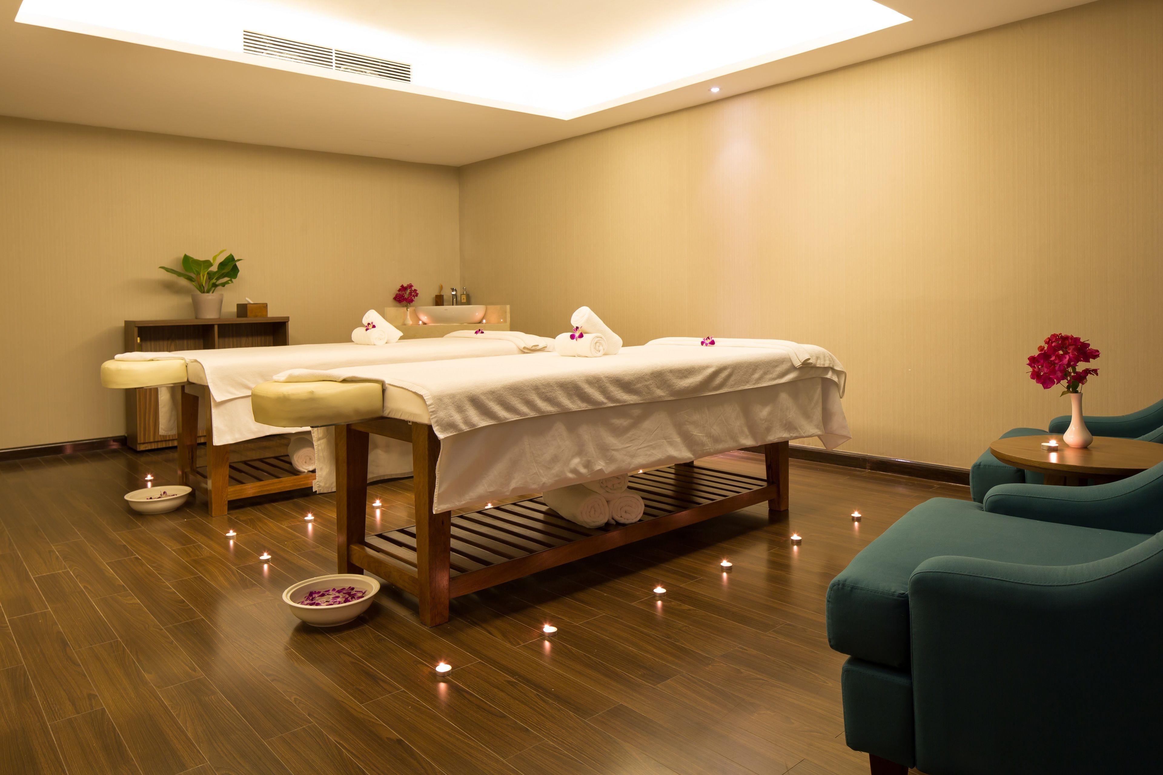 A spa room with two massage tables, a small plant, a bowl of bath salts, and teal chairs.