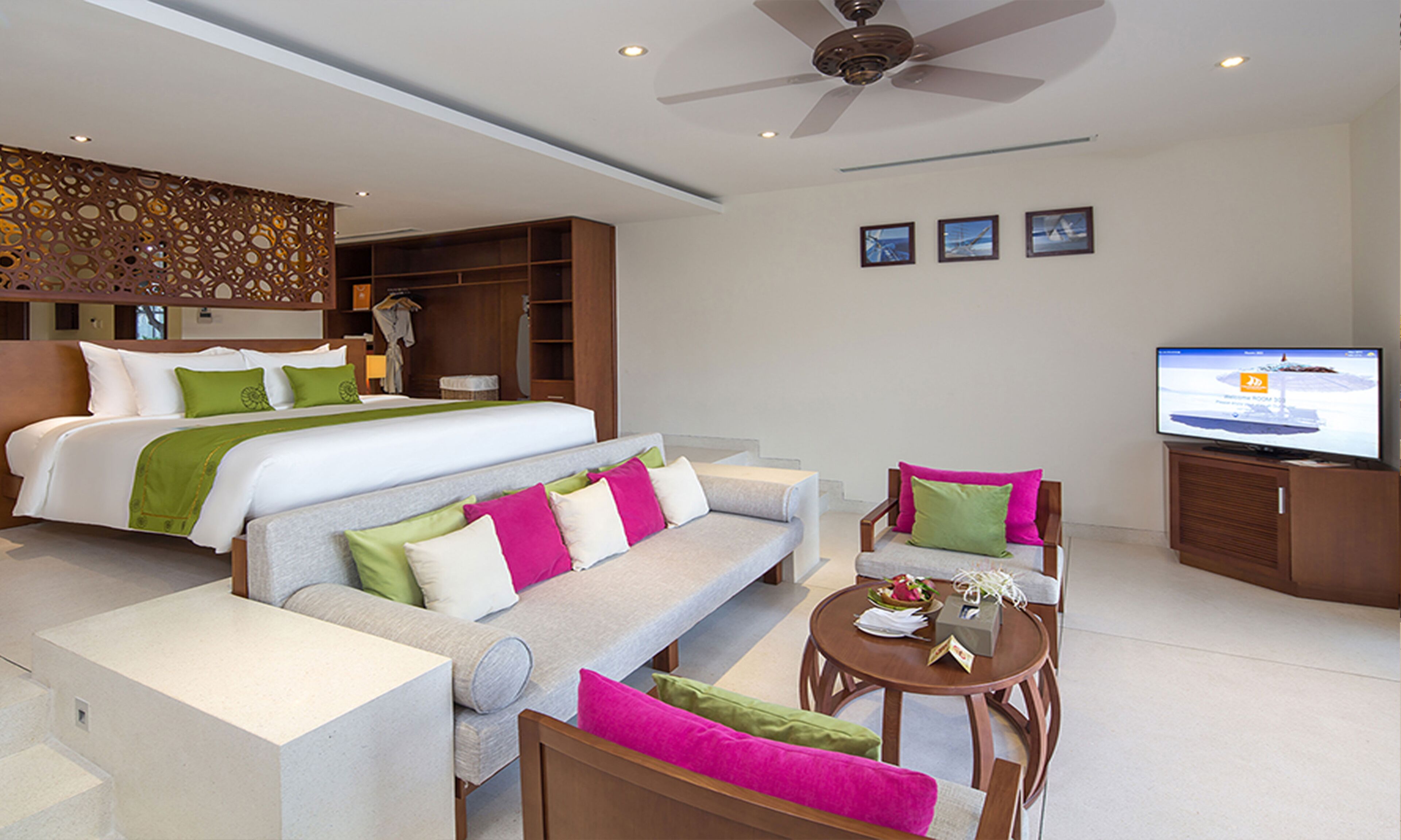 A modern hotel room with a large bed, a sofa, a dining table, and a television.