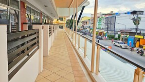 A balcony with a tiled floor, a railing, and a view of a busy street with vehicles and shops. - Dome Resort (Karon)