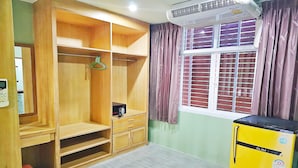 A room with a wooden wardrobe, a yellow refrigerator, a window with curtains, and an air conditioning unit. - Dome Resort (Karon)