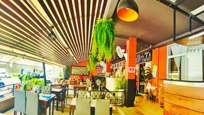 A restaurant with a modern interior, featuring striped ceiling, green plants, and a menu board. - Dome Resort (Karon)
