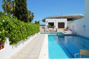 Una piscina al aire libre, sombrillas, sillones reclinables de piscina