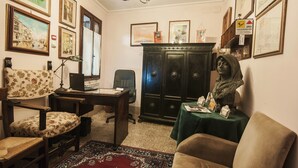 Una habitación con un escritorio, una silla y una estatua. En las paredes hay cuadros enmarcados y un candelabro.