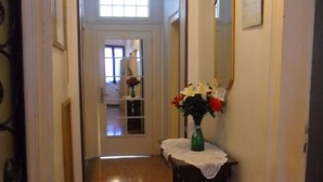 Un pasillo estrecho con suelo de madera, una mesita con un florero y un espejo en la pared.