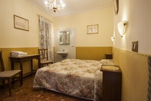 Un dormitorio con cama, escritorio, silla, mesita de noche, espejo y lavamanos.
