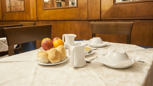 Una mesa de desayuno con pan, fruta y una jarrón.