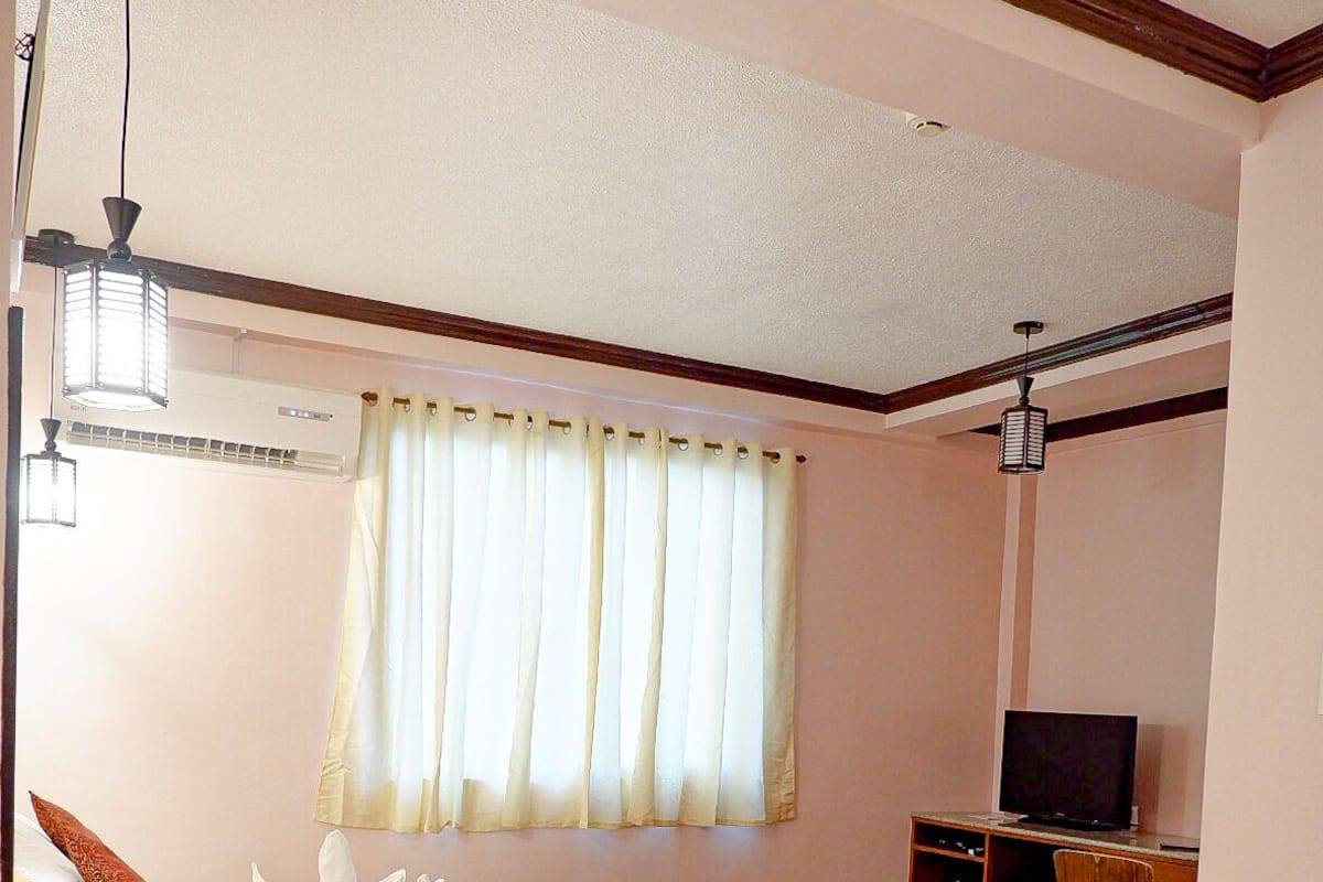 Ein Hotelzimmer mit zwei Betten, einem Schreibtisch, einem Fernseher und einem Fenster mit Vorhängen.