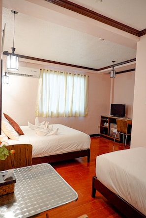 A hotel room with two beds, a desk, a television, and a window with curtains.