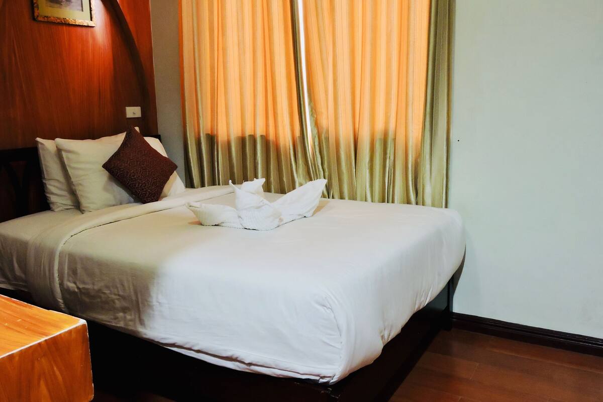 Ein Hotelzimmer mit einem ordentlich bezogenen Bett, einem hölzernen Kopfteil, einem gerahmten Bild an der Wand und einem Fenster mit Vorhängen.