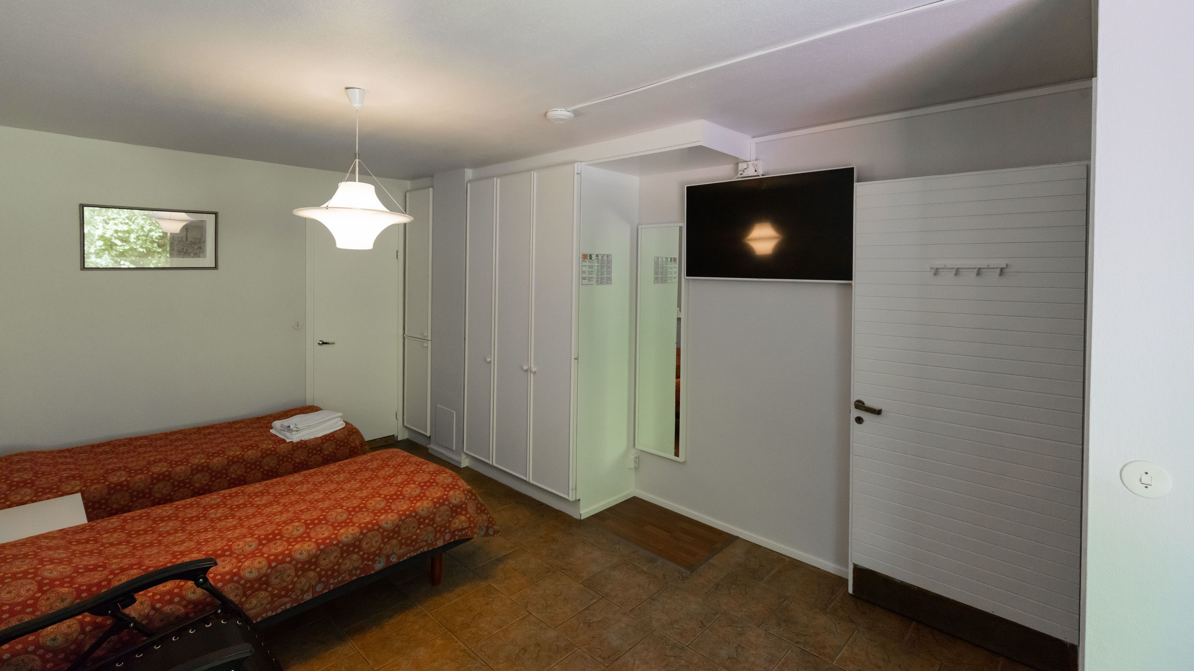 Une chambre avec deux lits, une télévision, une armoire et un luminaire au plafond.