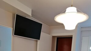A room with a tiled floor, a flat-screen TV mounted on a white wall, a red door, and a white door.