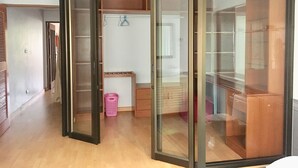 Une pièce dotée d’un placard avec une porte coulissante en verre, d’un plancher en bois, d’un panier à linge rose et d’une petite armoire en bois.