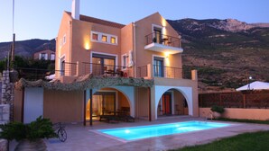 Une maison à deux étages avec une piscine, un espace salon extérieur et une vue sur les montagnes.