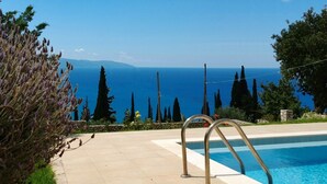 Une piscine avec vue sur la mer, entourée de cyprès et de plantes de lavande.