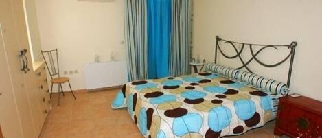 Un dormitorio con cama, una silla, un radiador y un ventanal con cortinas.
