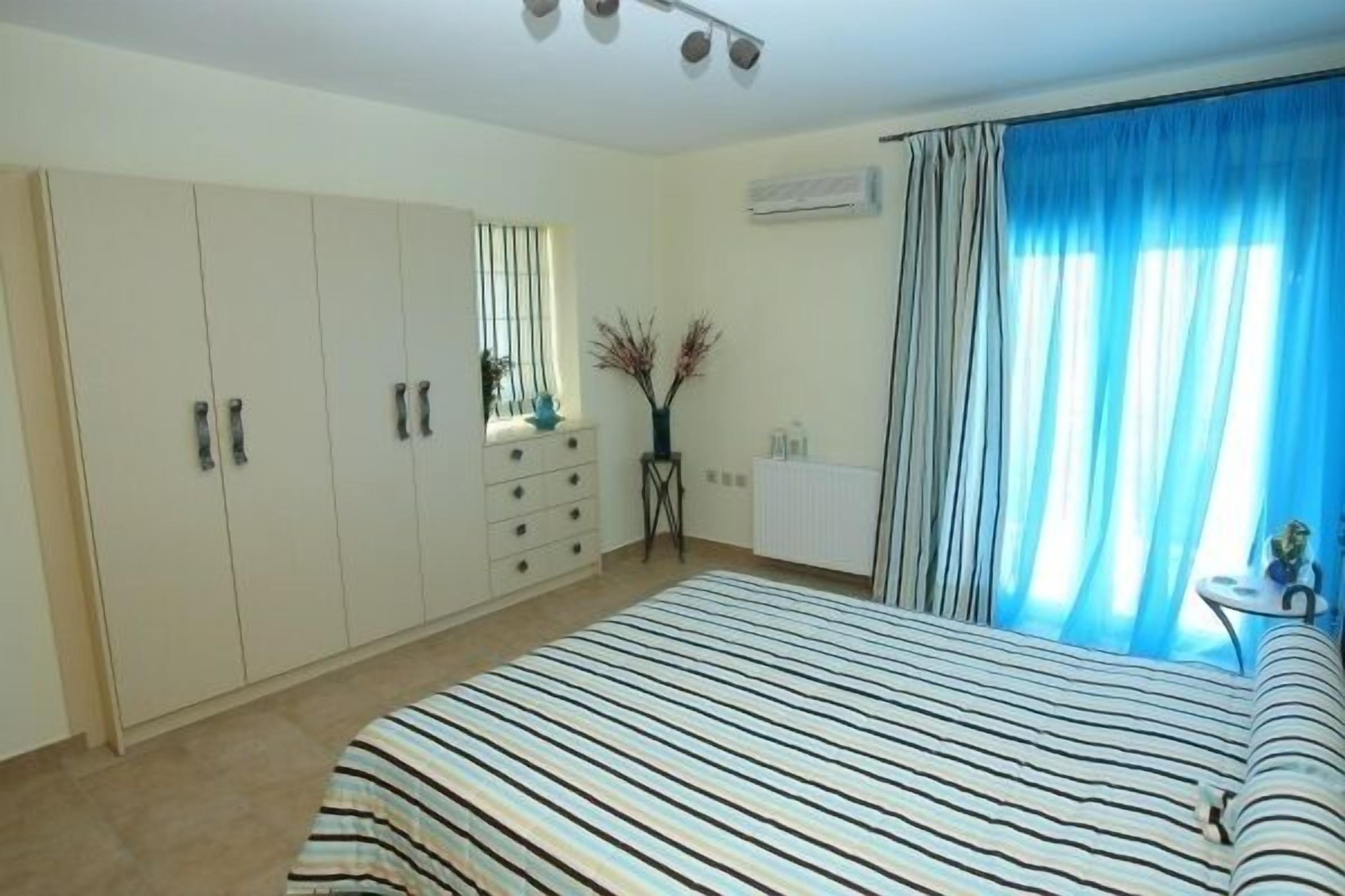 A bedroom with a bed, a wardrobe, a small table, and a window with curtains.