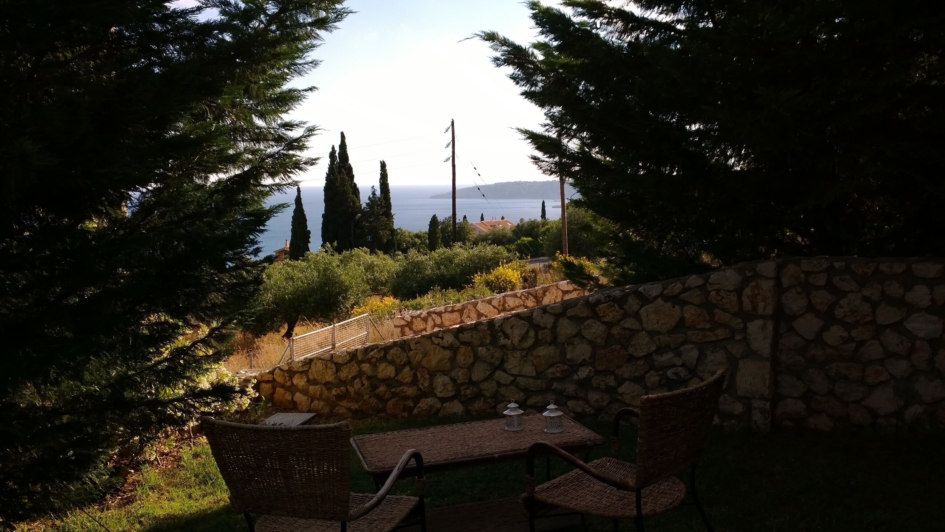 Un muro de piedra con un banco y una mesa, con vistas a un paisaje costero con árboles y el mar.