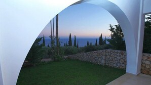 Une vue à travers une porte en arc donnant sur un jardin bien entretenu, avec un mur de pierre et une pelouse verdoyante, qui mène à une étendue d’eau.