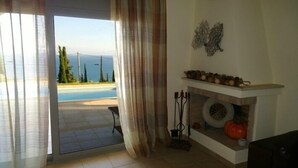 Une pièce avec vue sur une piscine et des arbres, une cheminée agrémentée d’un manteau décoratif et une porte ornée de rideaux légers.