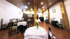 Un espace repas avec un plafond en bois, des tables recouvertes de nappes en dentelle, des chaises et un piano.